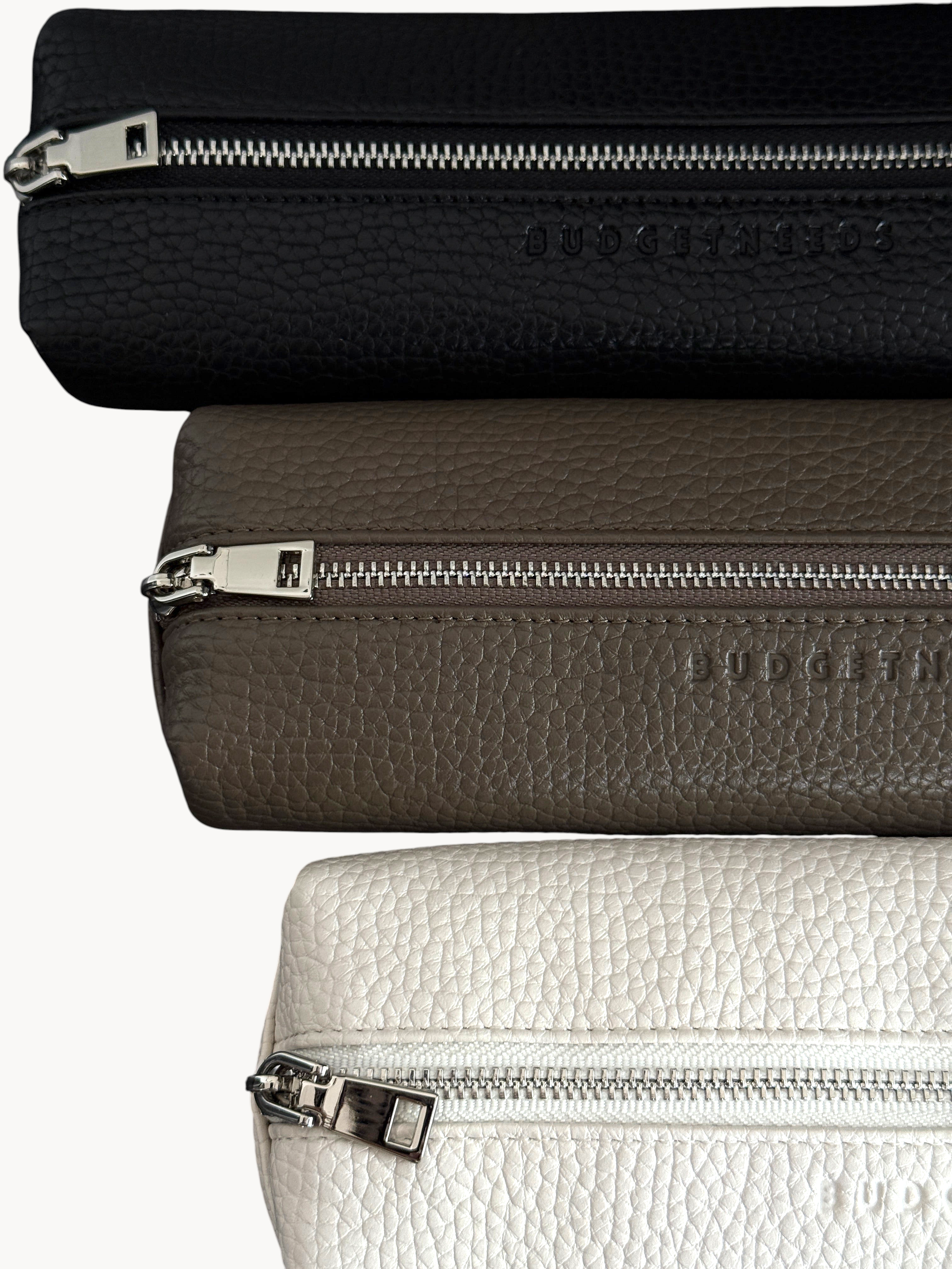 BUDGETNEEDS ™ vegan leather pencil cases in black, taupe, and beige with silver hardware and embossed brand logo.