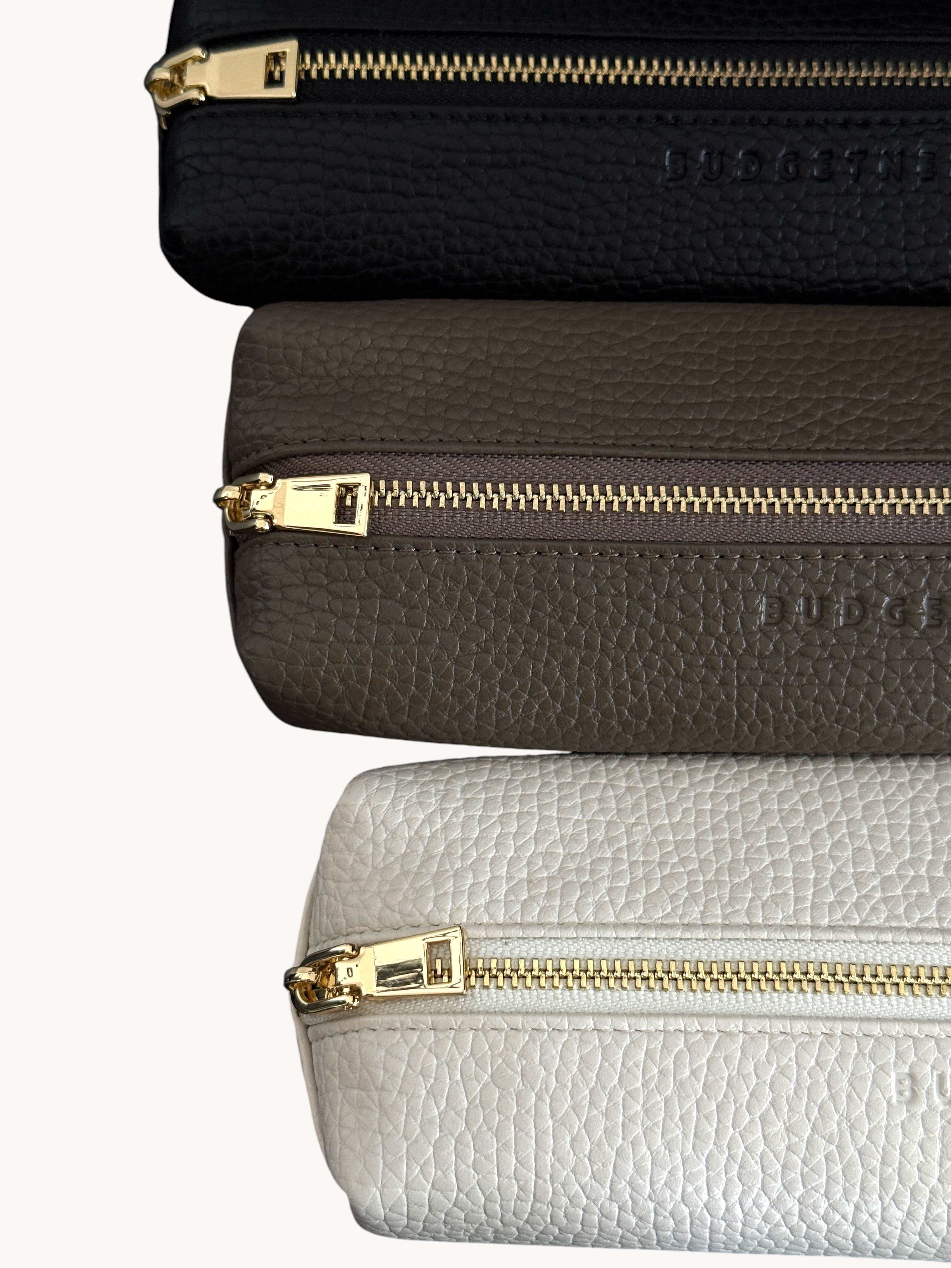 BUDGETNEEDS ™ vegan leather pencil cases in beige, taupe, and black with gold hardware on a dark background